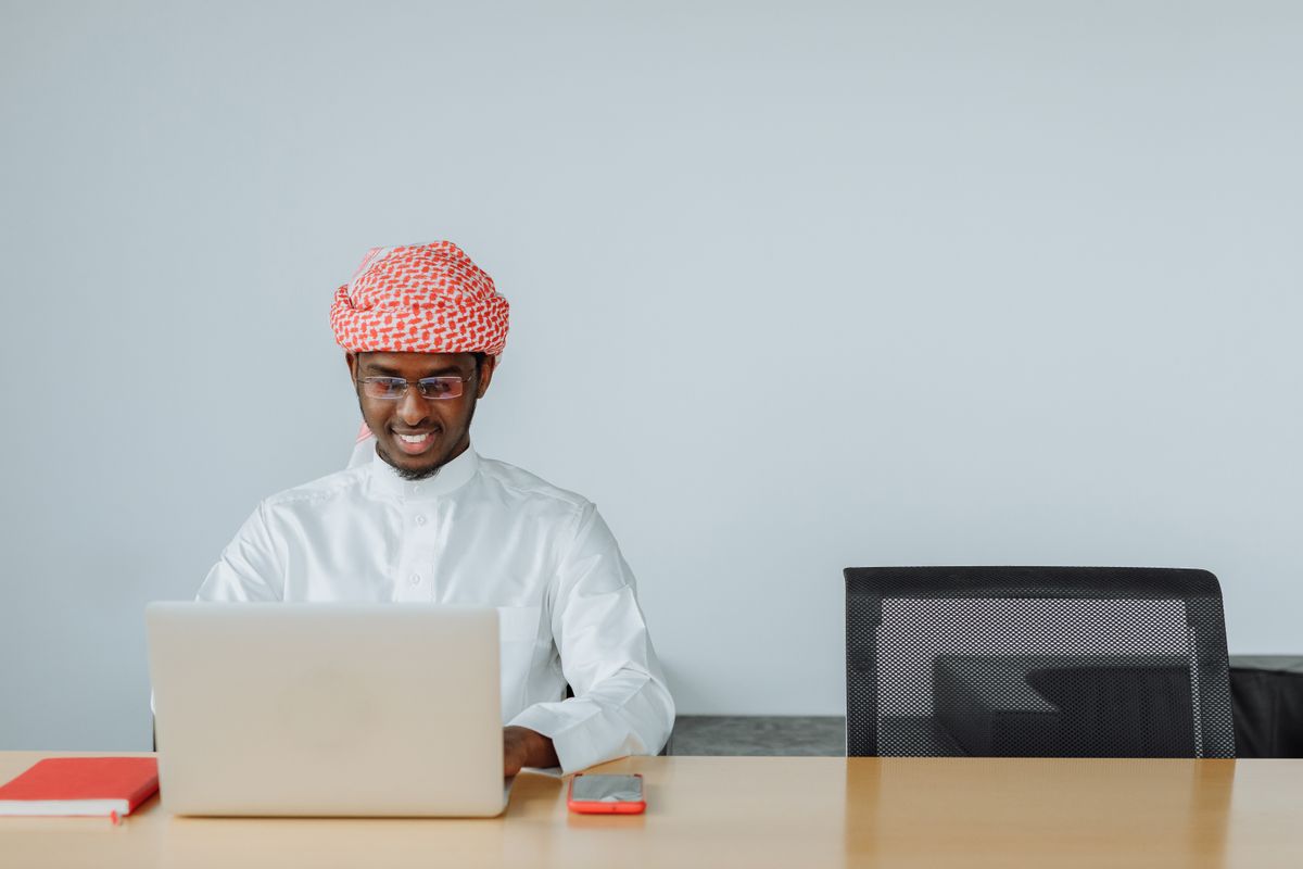 A businessman in traditional Emirati dress working at a laptop